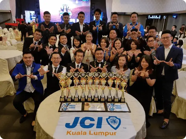 JCI Kuala Lumpur members cheering behind a table of trophies and certificates